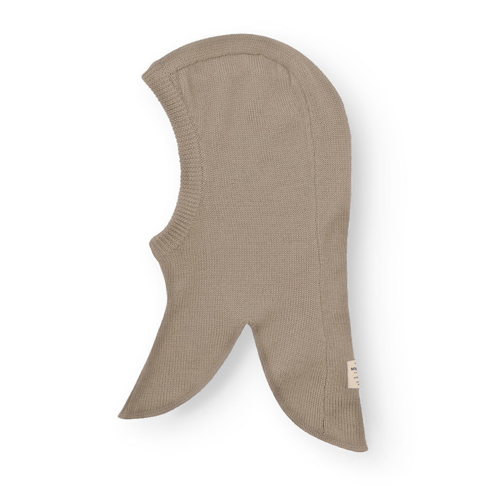 MATKEA let elefanthue i varm sandfarvet merinould, fotograferet forfra mod hvid baggrund. Her fremhæves den bløde strikstruktur, den ribstrikkede ansigtsåbning og de to spidse skulderflapper med MINI A TURE-label på den højre flap.