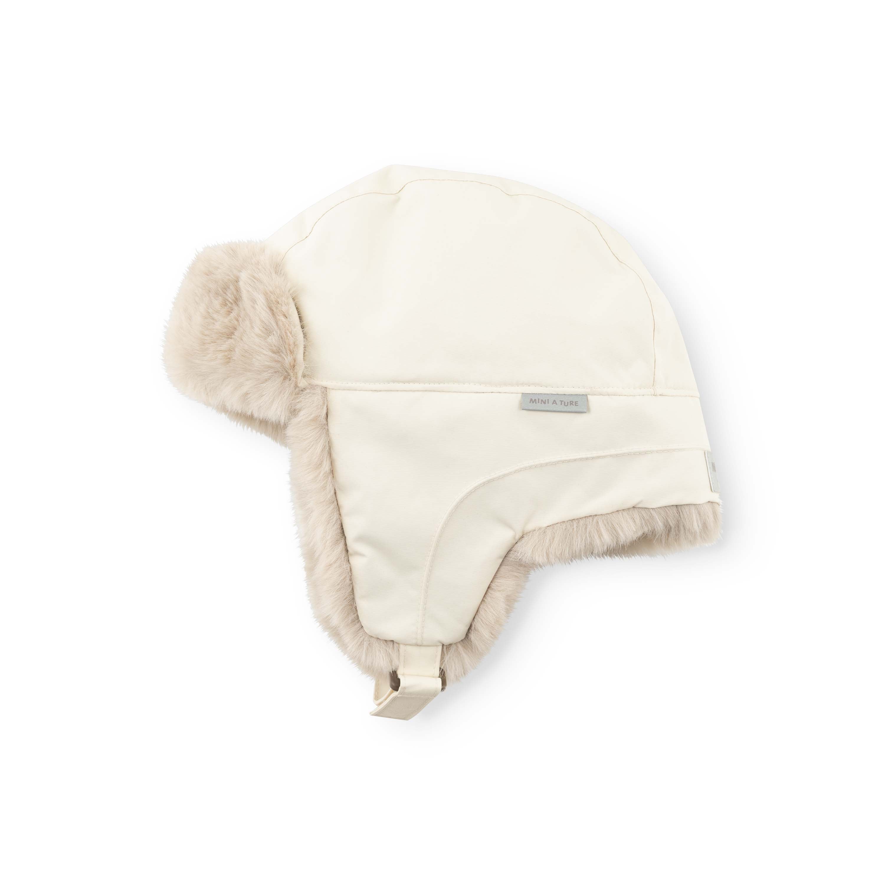 MATCRISTER teddyforet vinterhue i cremefarvet råhvid, fotograferet fra skrå side mod hvid baggrund. Det glatte yderstof af genanvendt nylon ses tydeligt på toppen og forsiden af huen, mens det varme, sandfarvede teddyfleece løber langs kanten af øreklapperne og ned mod den cremefarvede velcrostrop med metalspænde forneden.