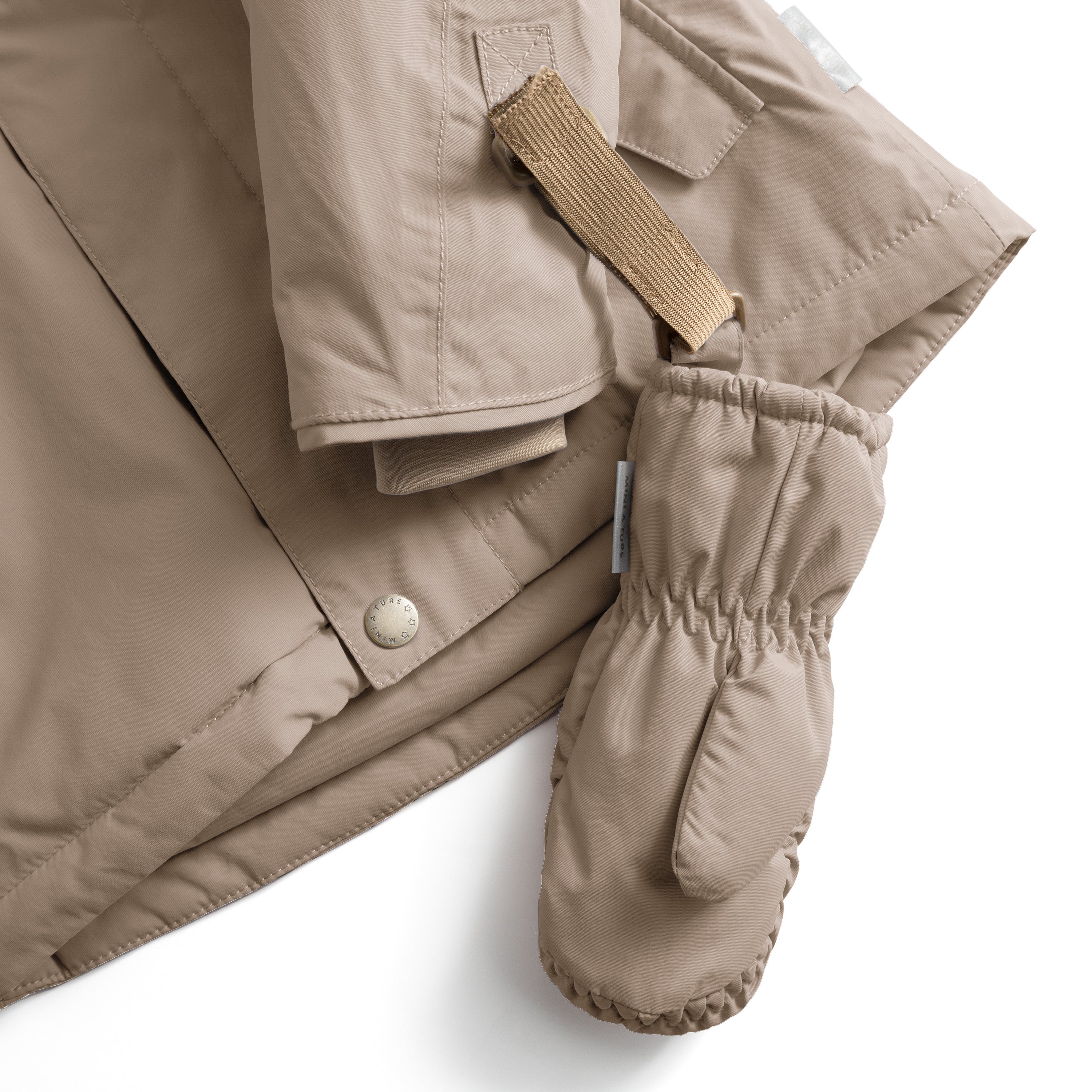 MATCORDT-fleeceforede luffer i varm sandbeige, fotograferet ovenfra ved siden af manchetten på en matchende vinterjakke. Her er den sandfarvede velcrostrop ført gennem jakkens manchetflig og holder luffen på plads. Både luffens rynkede elastik ved håndleddet og jakkens trykknap ved manchetten er tydeligt synlige.