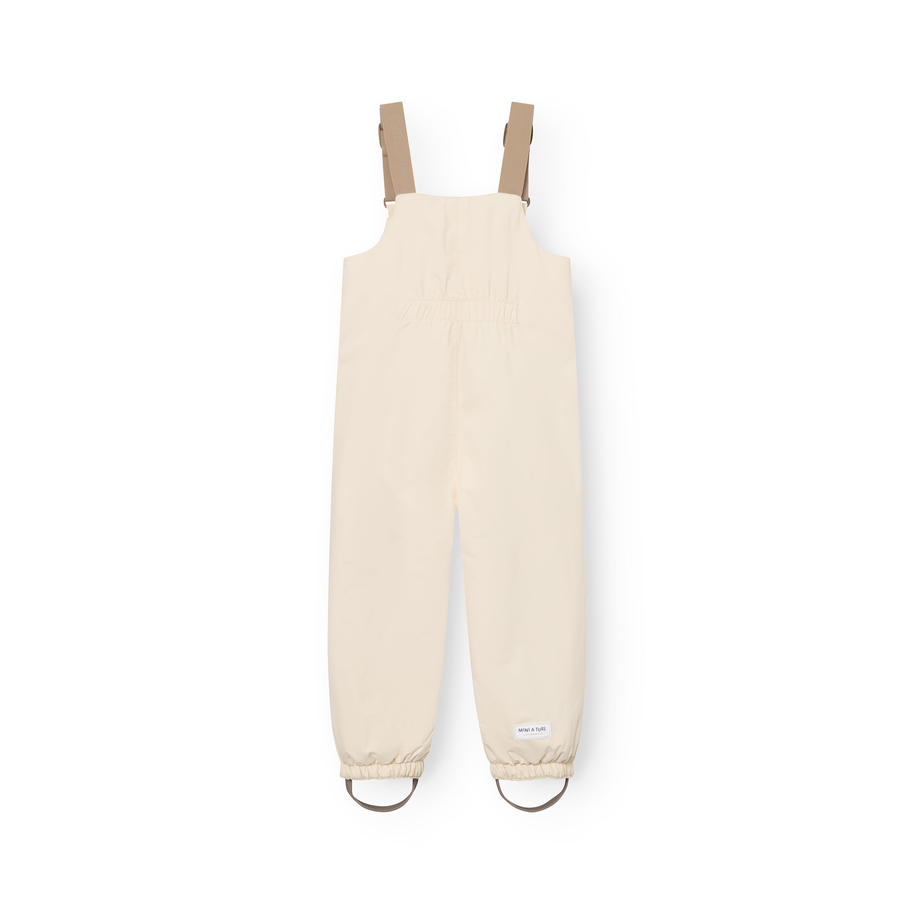 MATWALENTEX overtræksbukser til børn i lys råhvid, set bagfra uden model. Bukserne har et sandfarvet brystparti, beige justerbare seler og elastiske bukseben med fodstropper i matchende beige.