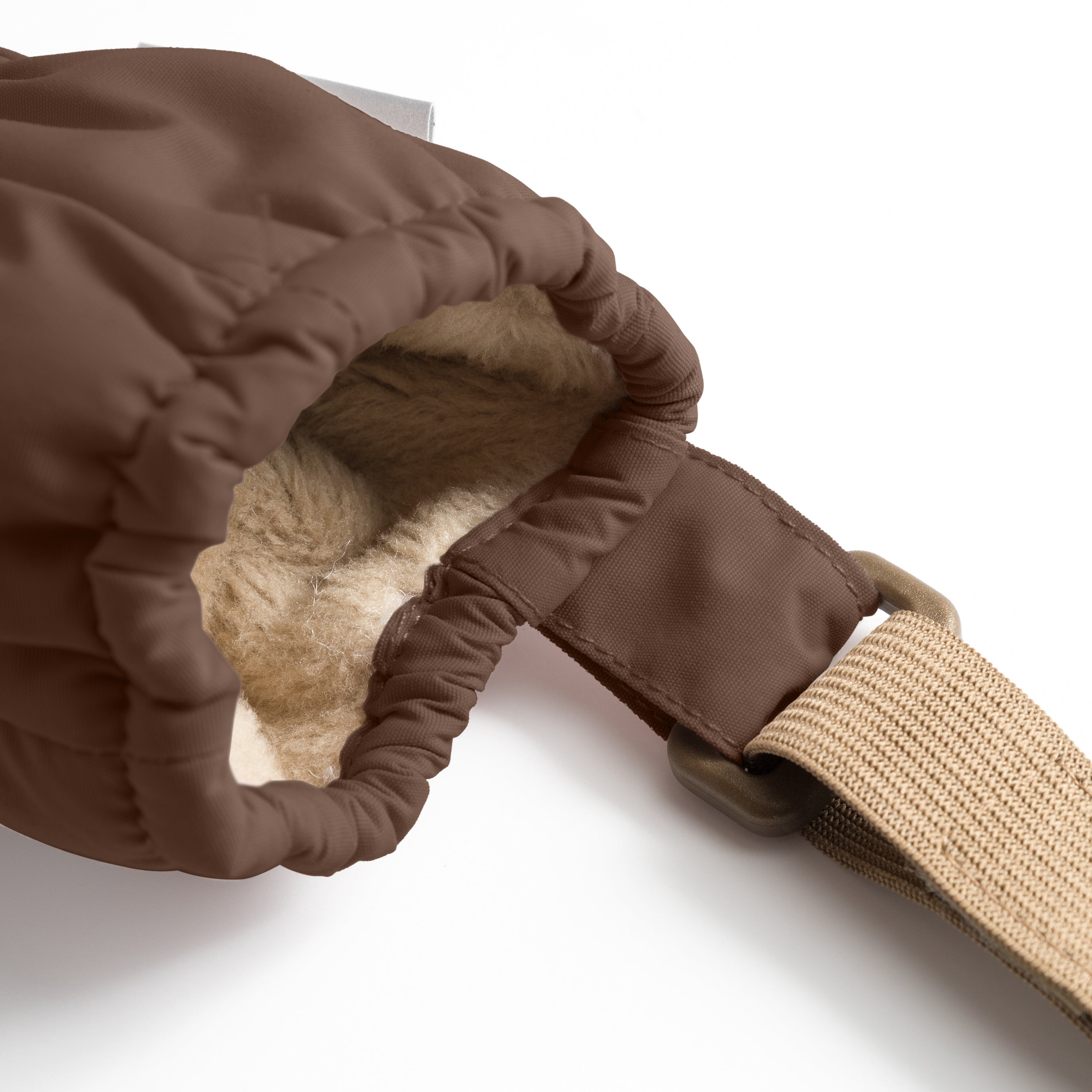 Indersiden af en MATCORDT-fleeceforet luffer i chokoladebrun, fotograferet tæt på fra siden, så det varme, beige fleecefór og den rynkede indre elastik ved åbningen er tydeligt synlige. En bred, sandfarvet velcrostrop løber vandret fra manchetten mod højre i billedet.