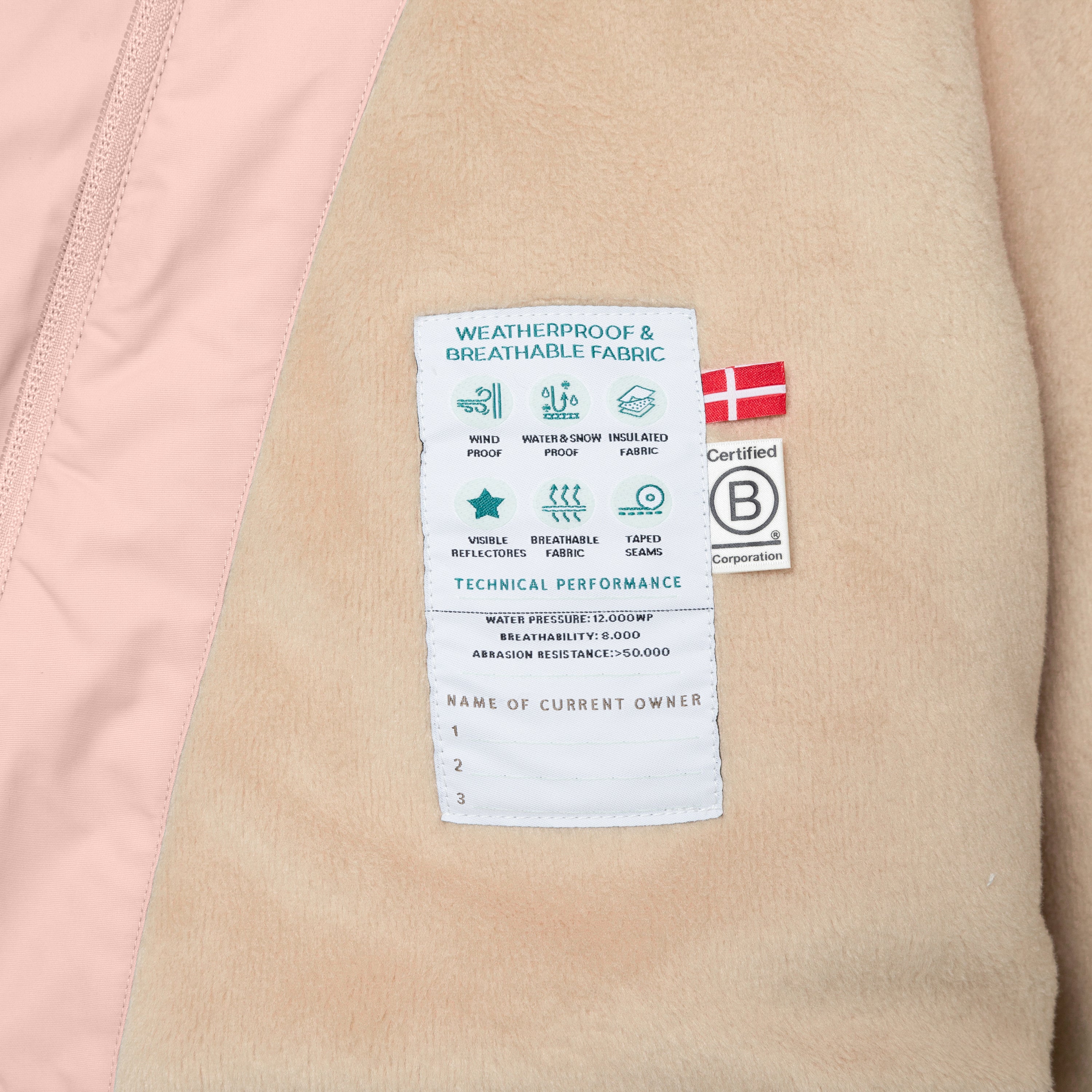 Nærbillede af indersiden af en børnevinterjakke med blød fleeceforing og et teknisk mærkat, der viser vigtige specifikationer som vandtæthed, åndbarhed og slidstyrke samt et B Corp-certificeringsmærke.